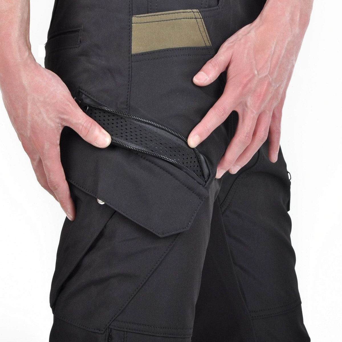 Hands pulling open a zipped thigh pocket on black riding pants, perforated black mesh lining visible behind the zip, an olive panel above and a stitched flap pocket below