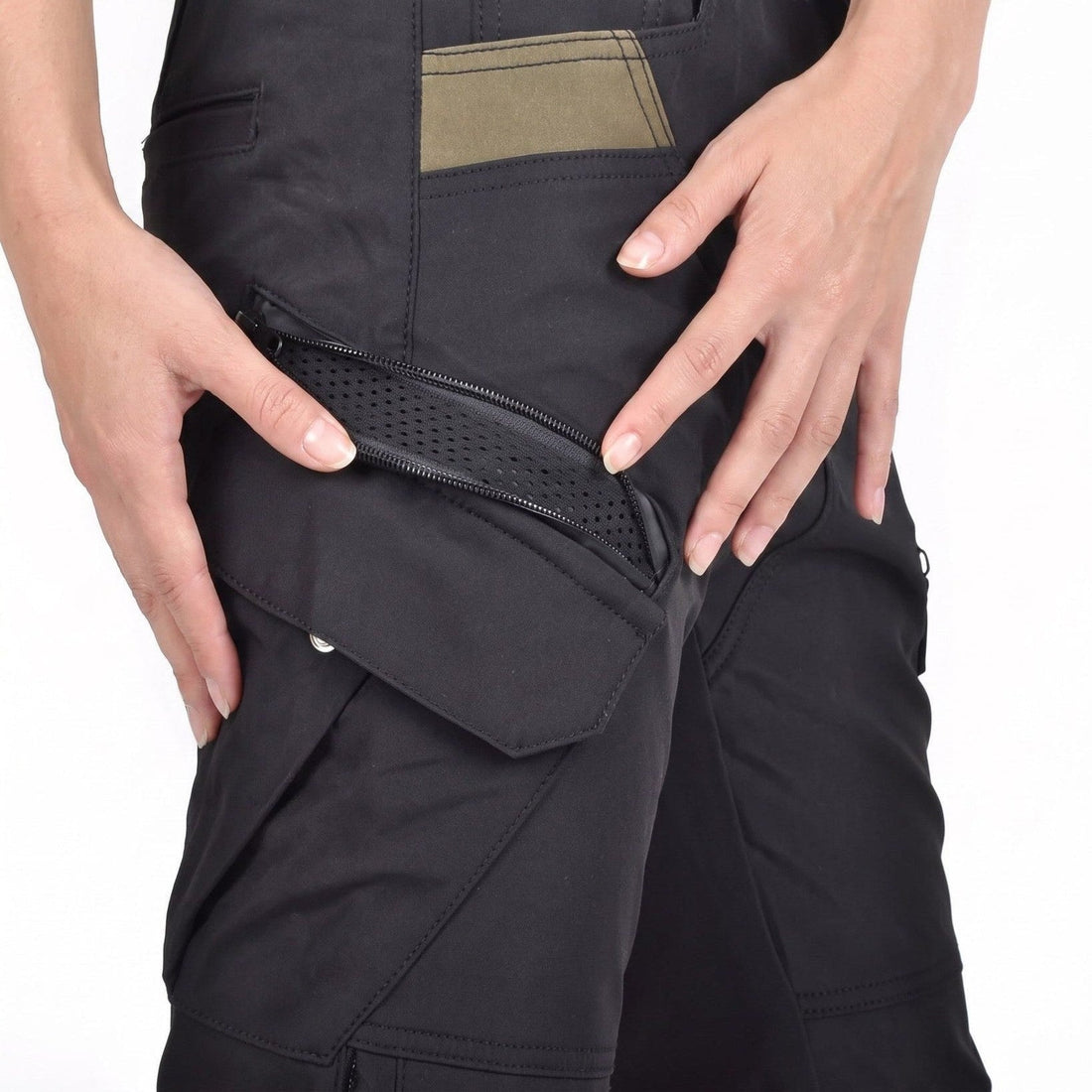 Close-up of black riding pants at the thigh, two hands holding a diagonal zip open over perforated black mesh, with a snap flap pocket below and an olive panel at the top of the frame