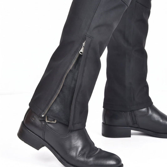 Black riding pants with an ankle zip open over black mesh, worn above a black leather boot in mid-stride on a white background