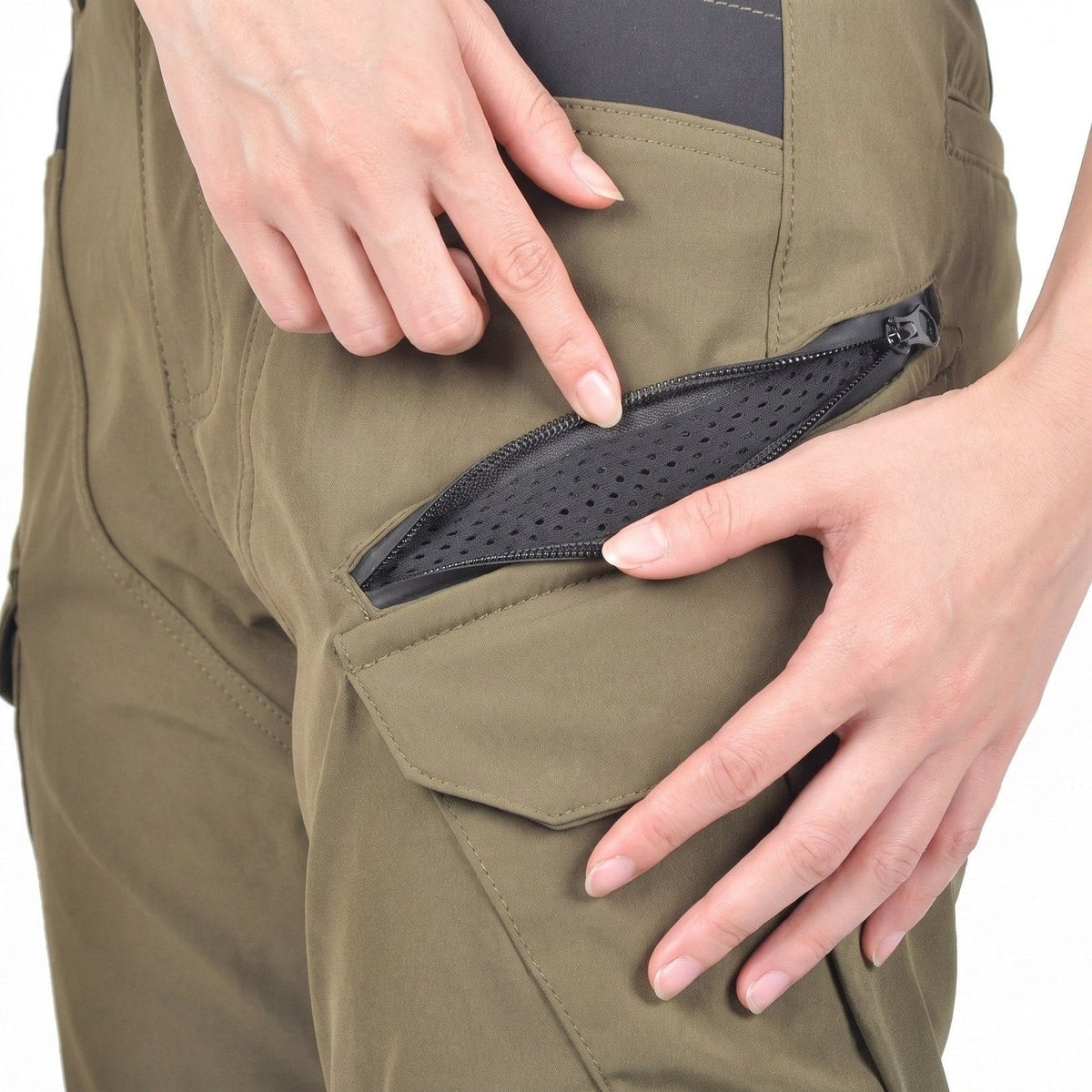 Fingers holding open a zipped thigh vent on army green cargo riding pants, perforated black mesh lining visible behind the zip, a dark panel at the top and a flap pocket below