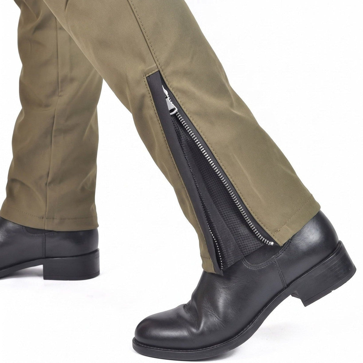 Olive riding pants with a zip opening and a black mesh panel at the ankle, worn over a black leather boot, shown mid-stride against a white background